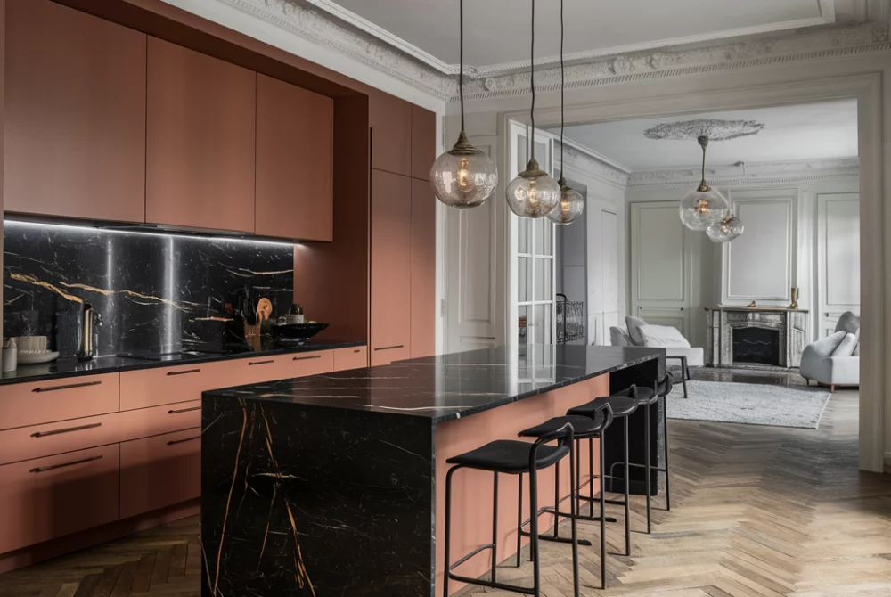 Cuisine contemporaine avec îlot en marbre noir veiné, façades terracotta mates, parquet en chevrons et moulures haussmanniennes.